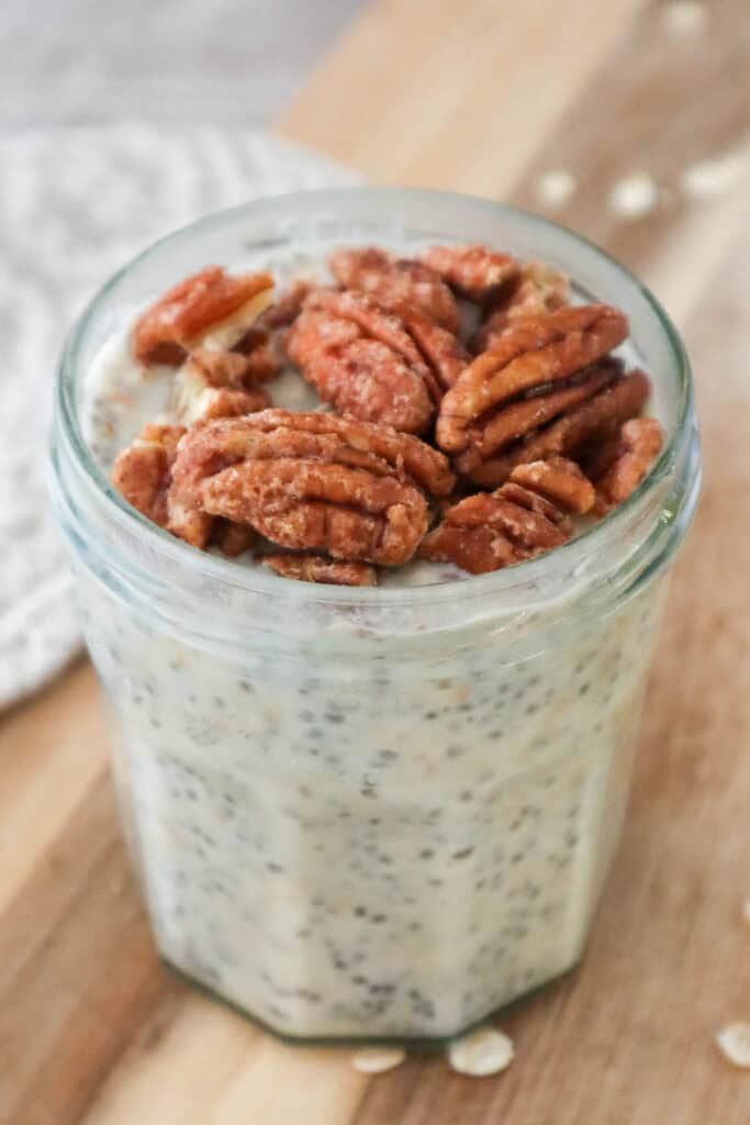 Maple overnight oats with maple pecans in glass jar on wooden board.