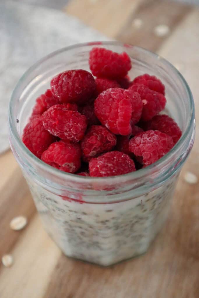Overnight oats made with maple syrup topped with raspberries in a glass jar on a wooden board.