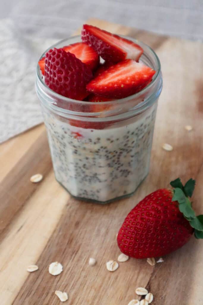 Maple overnight oats with chia seeds topped with fresh chopped strawberries on a wooden board.