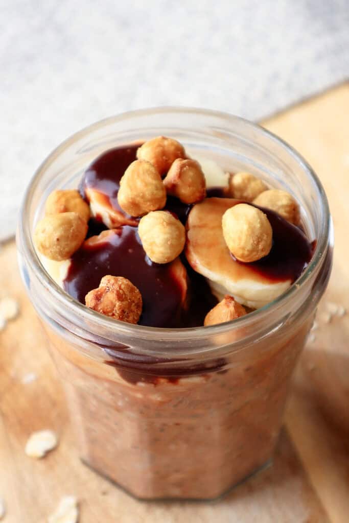 Overnight oats in glass jar topped with bananas, hazelnuts and nutella sauce.