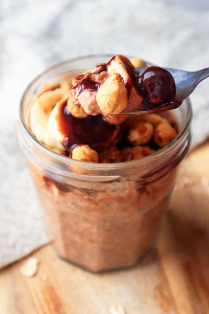 Spoonful of overnight oats topped with Nutella, bananas and hazelnuts.