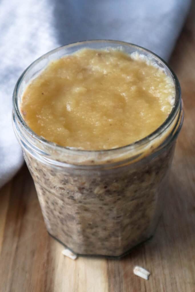 Oats with applesauce topping in a glass jam jar on a wooden board.