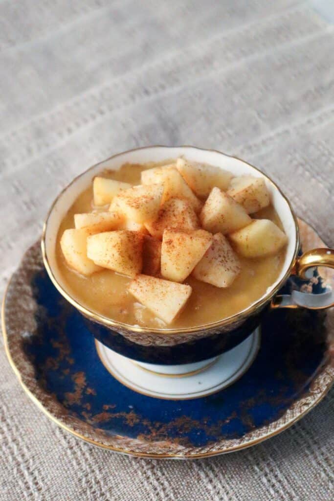 Pretty blue and gold teacup filled with overnight oats, applesauce and diced apples.