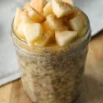 Applesauce overnight oats topped with chopped apples in a glass jam jar that is sitting on a wooden cutting board.