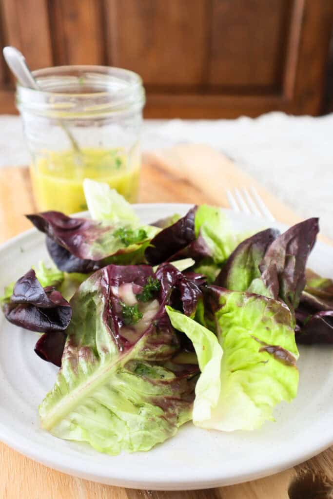 Butter lettuce on beige plate with salad dressing in glass jar in background.
