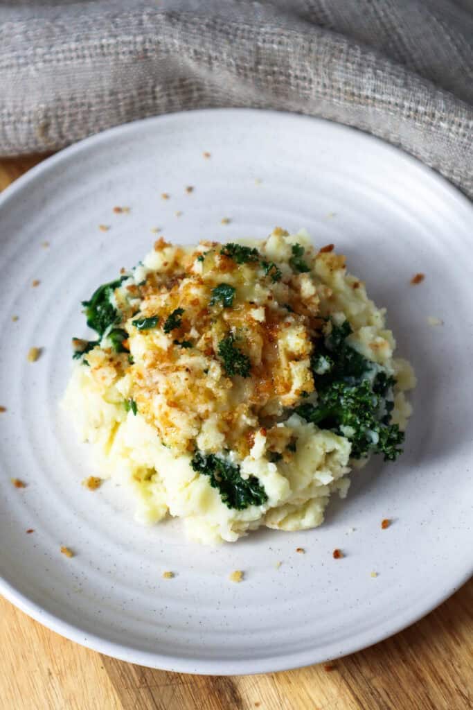 Cottage cheese with mashed potatoes and kale topped with panko crumbs on a beige plate.