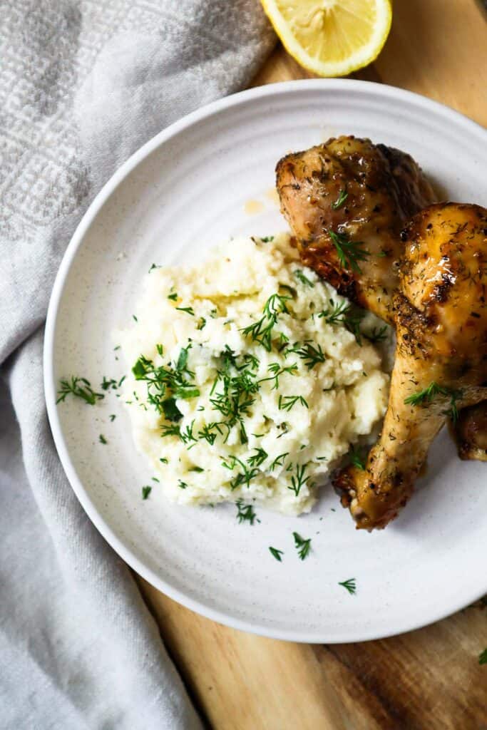 Cottage cheese mashed potatoes with two lemon pepper chicken drumsticks on beige plate.