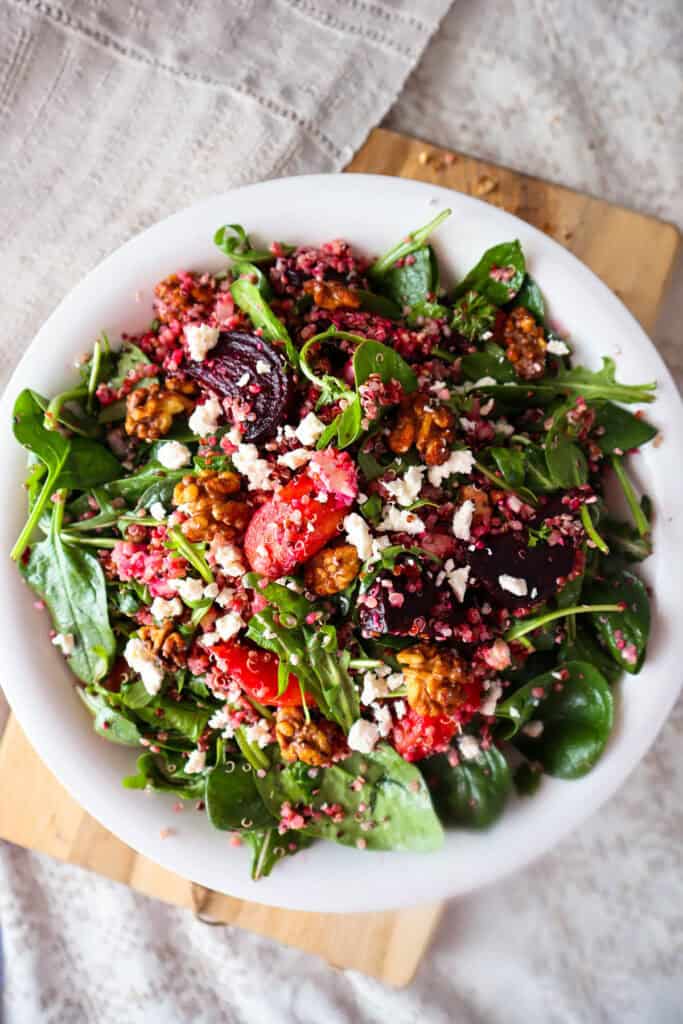 Bowl of fall quinoa salad with beets, carrots, feta, walnuts, baby spinach, and arugula.