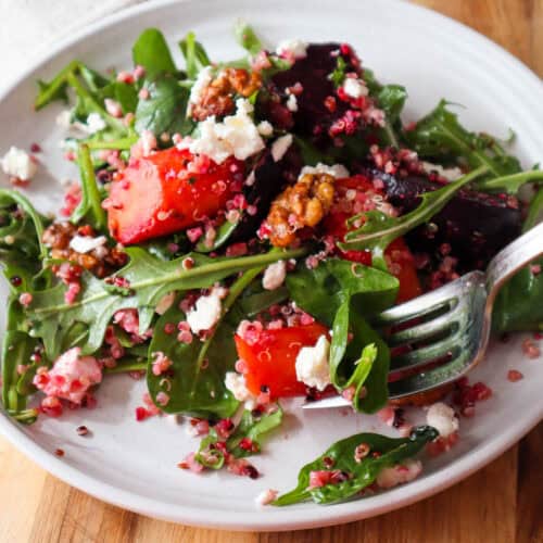 Fall quinoa salad with roasted beets and carrots, baby spinach, arugula, feta and walnuts on a small beige plate and a forkful of salad.