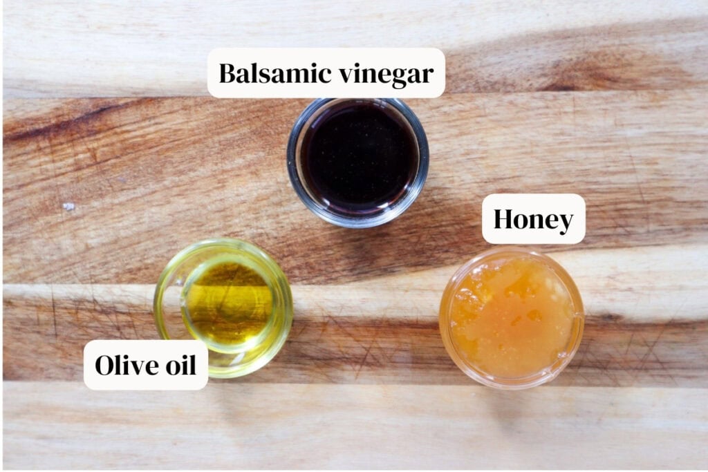 Honey, balsamic vinegar, olive oil in small glass bowls on wooden board.