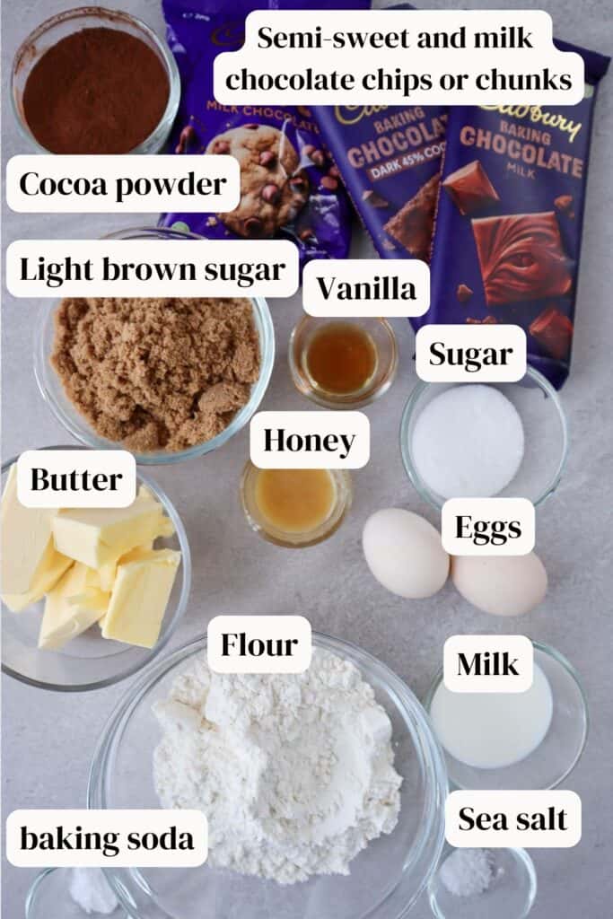 Semi-sweet and milk chocolate bars and bits, light brown sugar, honey, white sugar, butter, flour, milk, vanilla, sea salt, baking soda in small glass bowls and two eggs.