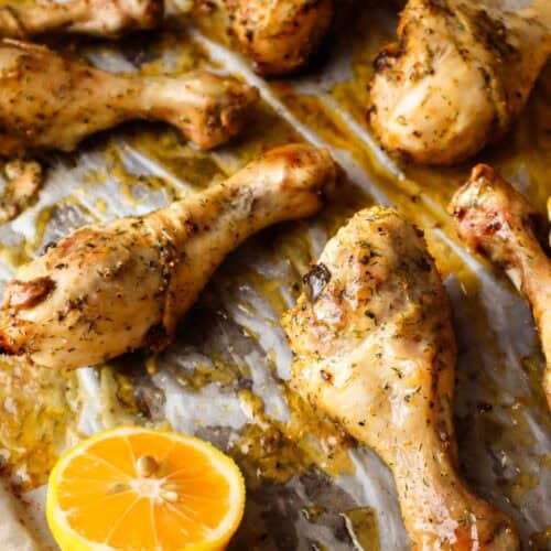 Five lemon pepper chicken drumsticks on parchment paper with half of a lemon.