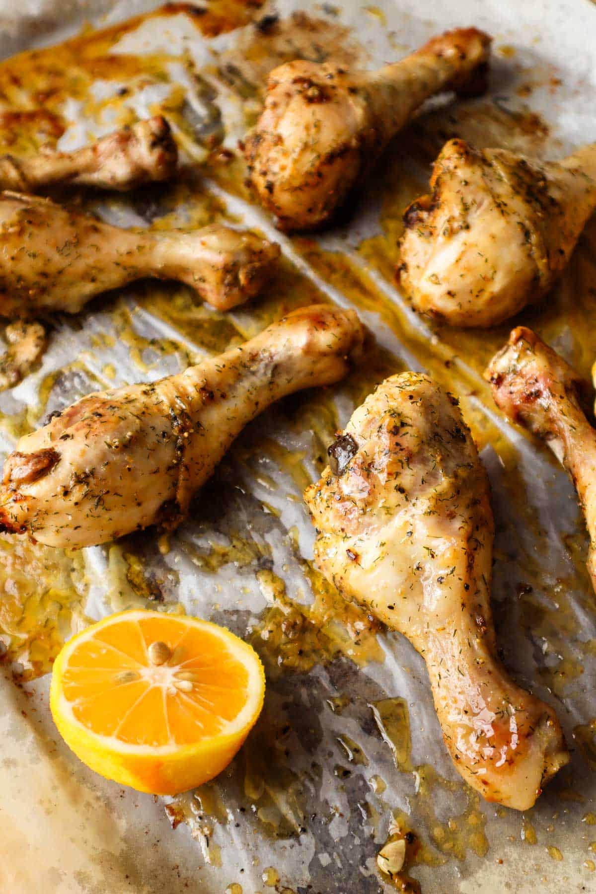 Five lemon pepper chicken drumsticks on parchment paper with half of a lemon.