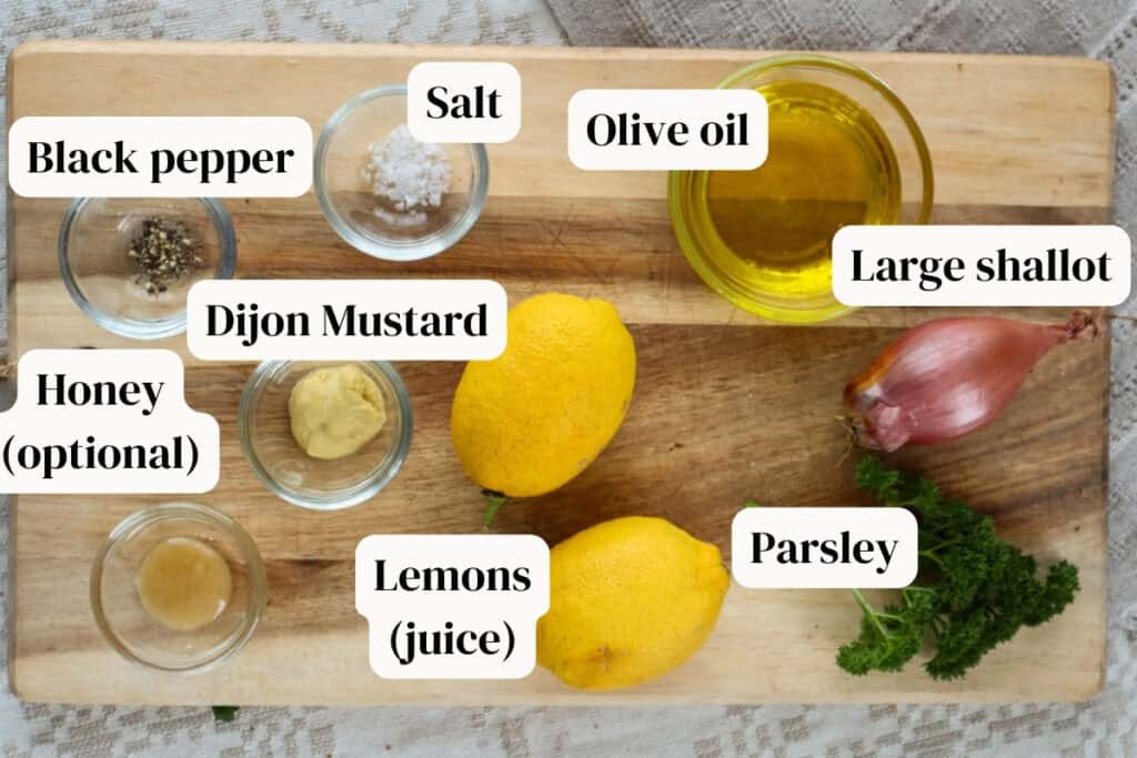 Lemons, olive oil, shallot, black pepper, salt, dijon mustard, honey in small glass bowls on a wooden board with parsley.