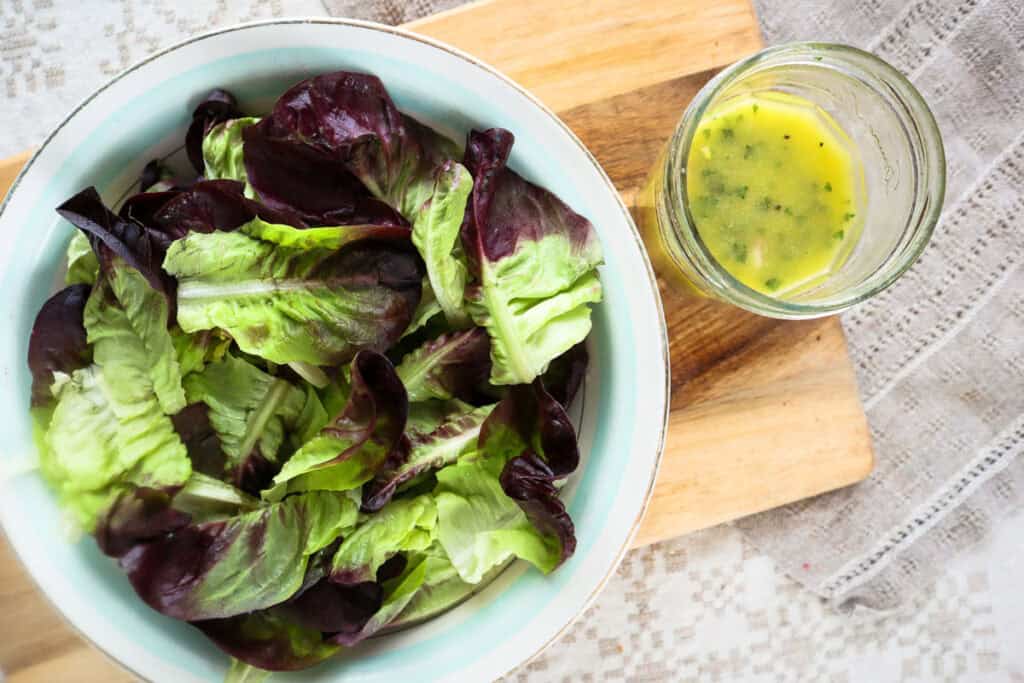 Butter lettuce in a white bowl with yellow dressing next to it in a glass jar.