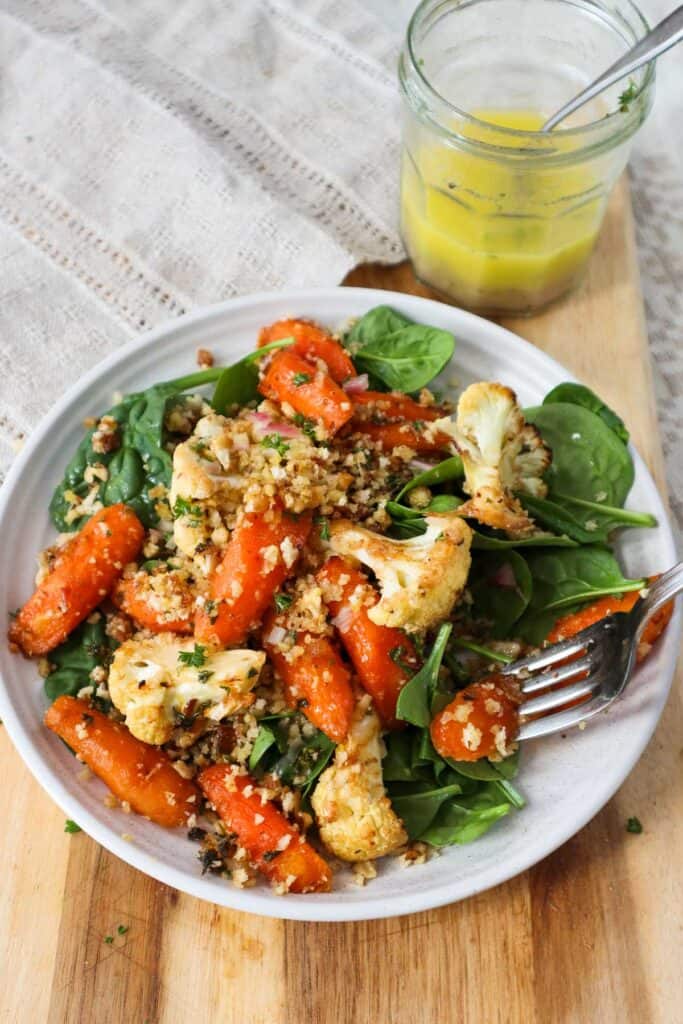 Roasted carrots and cauliflower with spinach and French dressing in jar on the side.