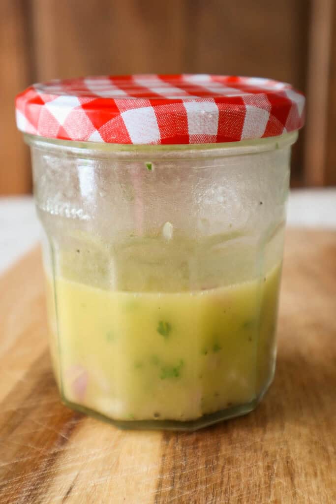 Lemon shallot vinaigrette in glass jar with red top on wooden board.