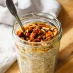 Overnight oats with maple syrup and chopped pecans in a jam jar with a spoon.