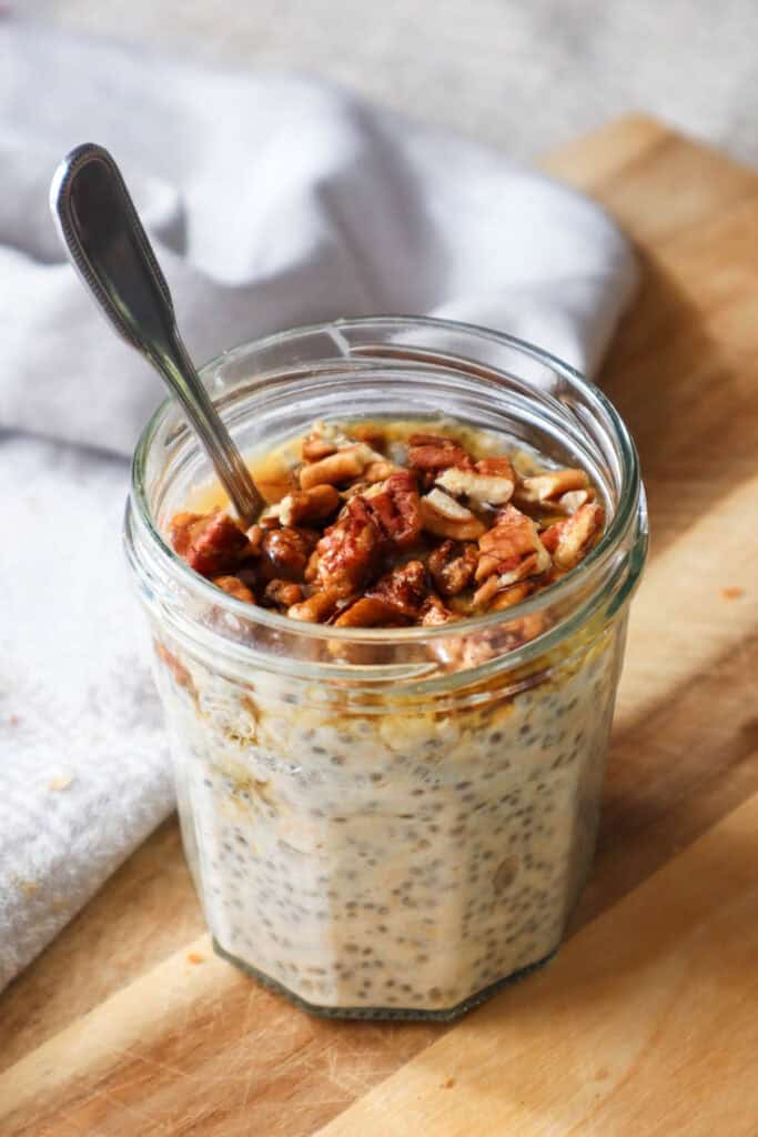 Overnight oats with maple syrup and chopped pecans in a jam jar with a spoon.