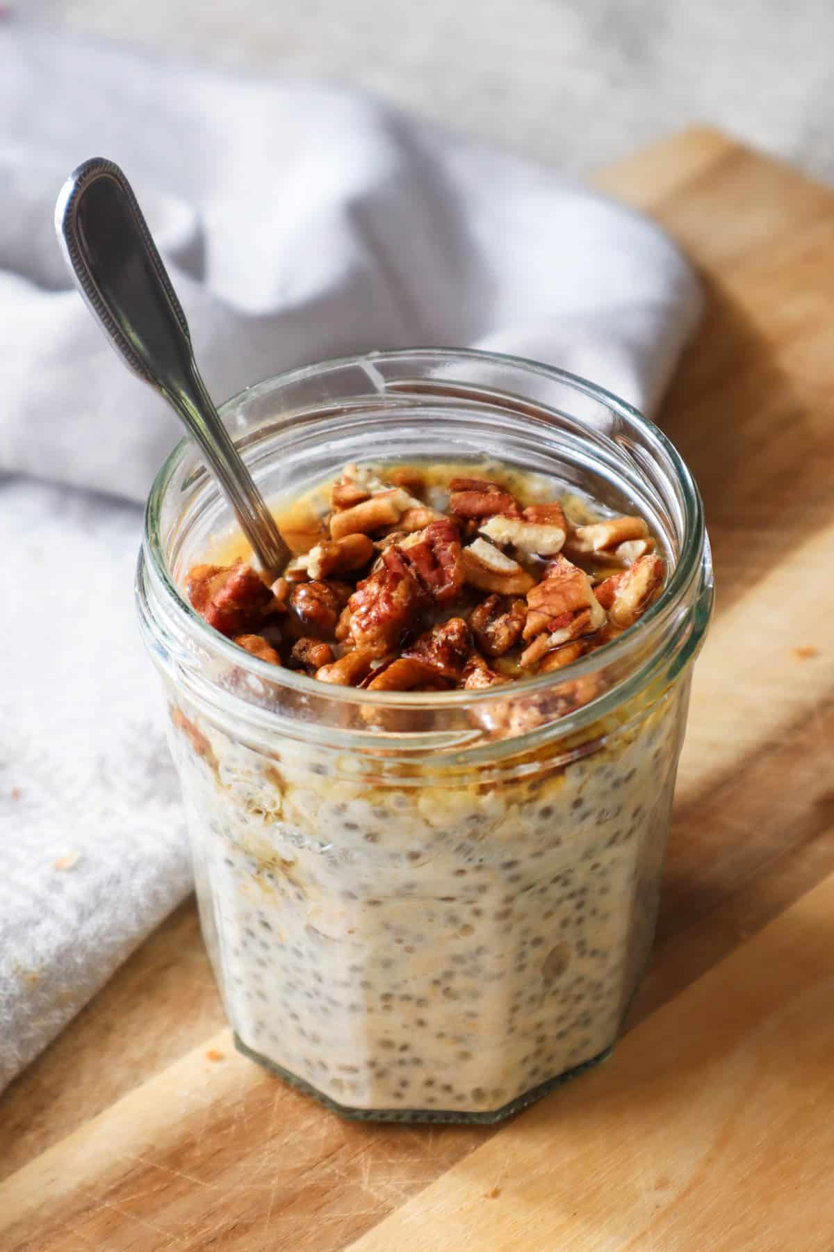 Overnight oats with maple syrup and chopped pecans in a jam jar with a spoon.
