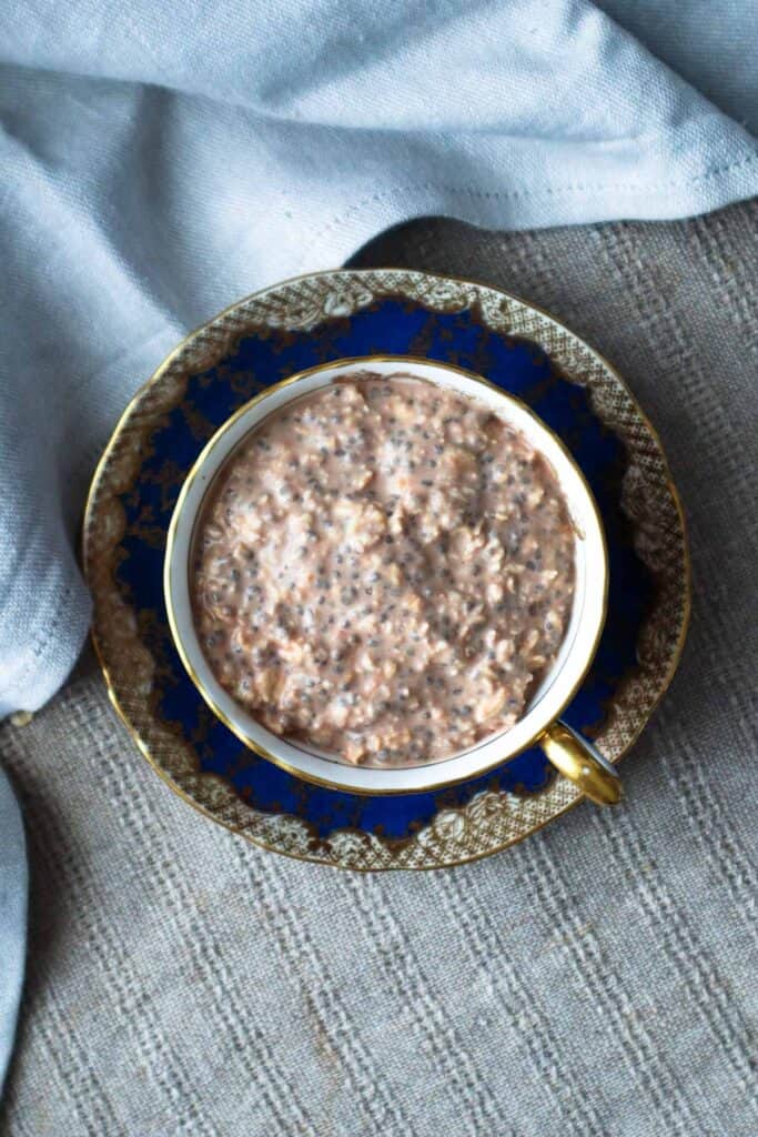 Overhead view of Nutella overnight oats in a blue teacup on a linen tablecloth.
