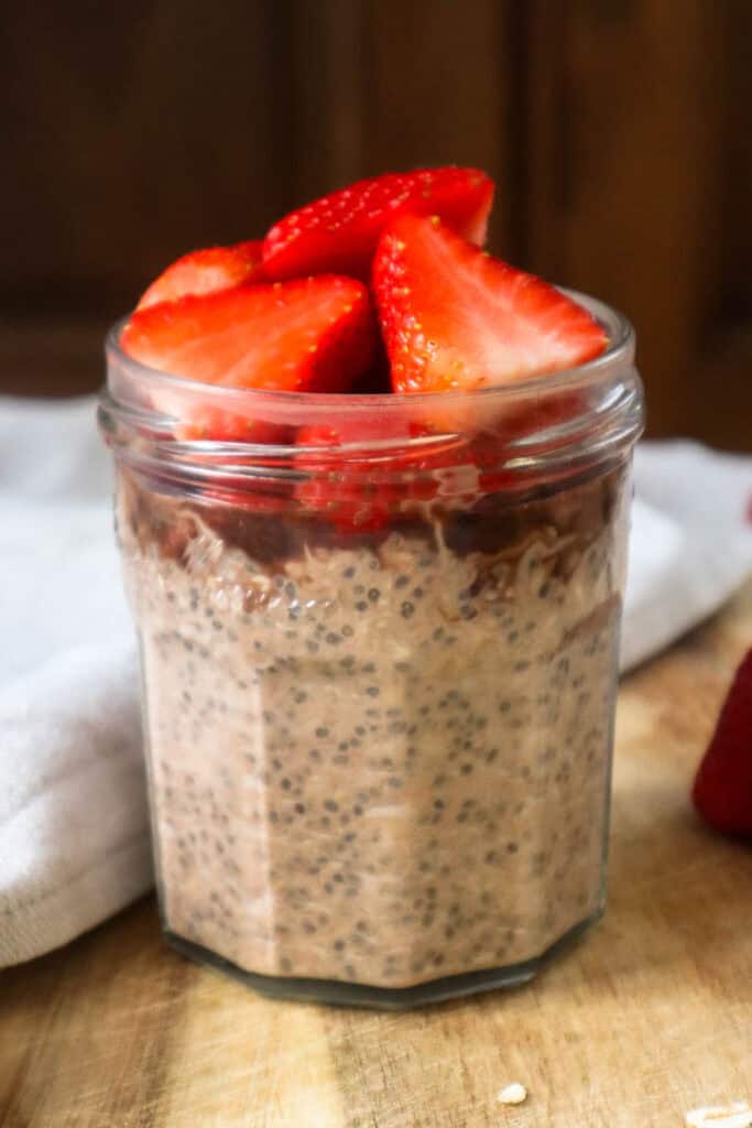 Nutella overnight oats topped with sliced strawberries on a wooden board.