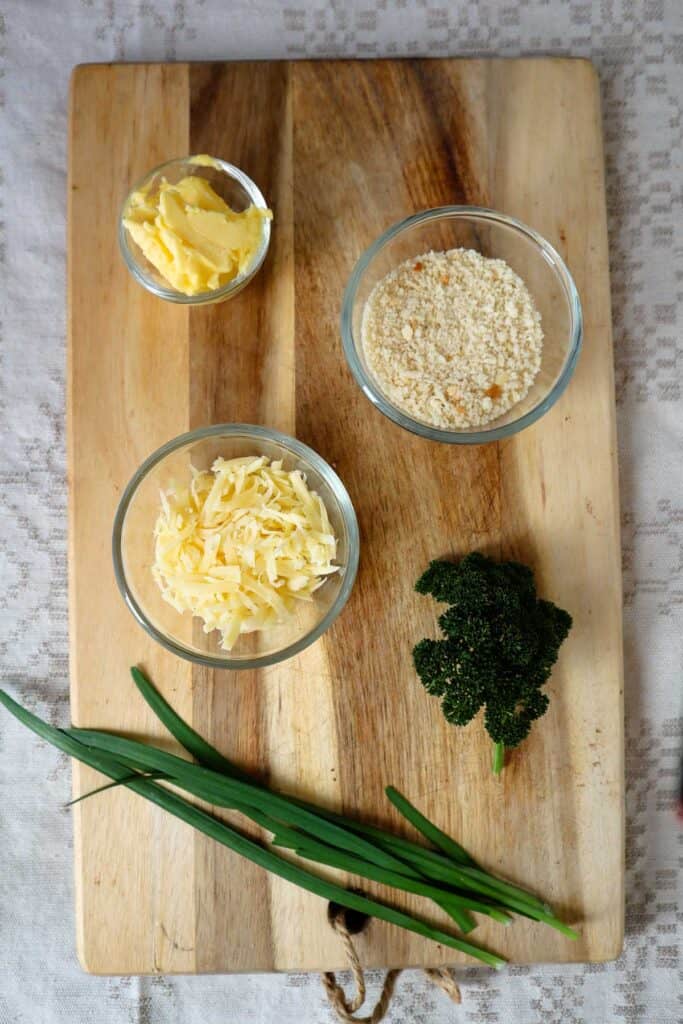 Panko crumbs, butter, herbs, grated cheese in small glass bowls on wooden board.