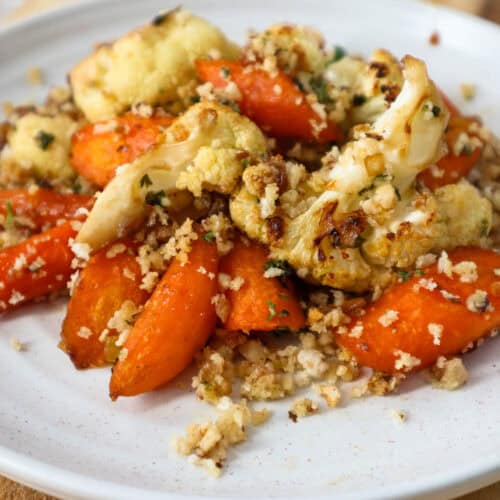 Roasted carrots and cauliflower with walnut panko crumbs on a beige plate.