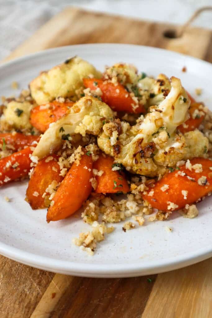 Roasted carrots and cauliflower with walnut panko crumbs on a beige plate.