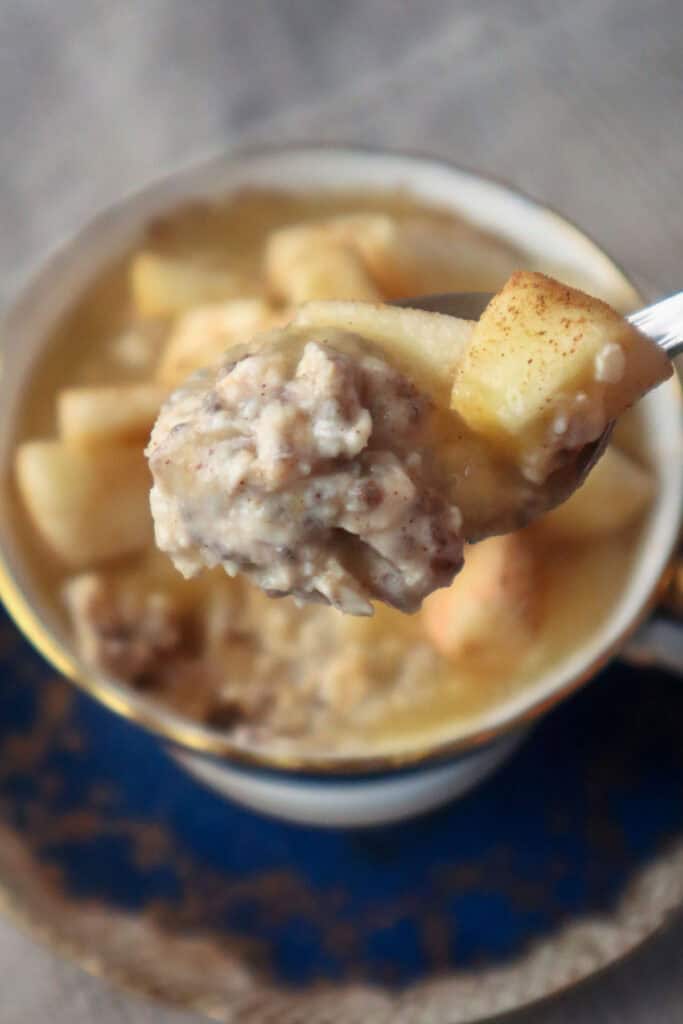 Spoonful of breakfast oats with chopped apple and a teacup in the background.