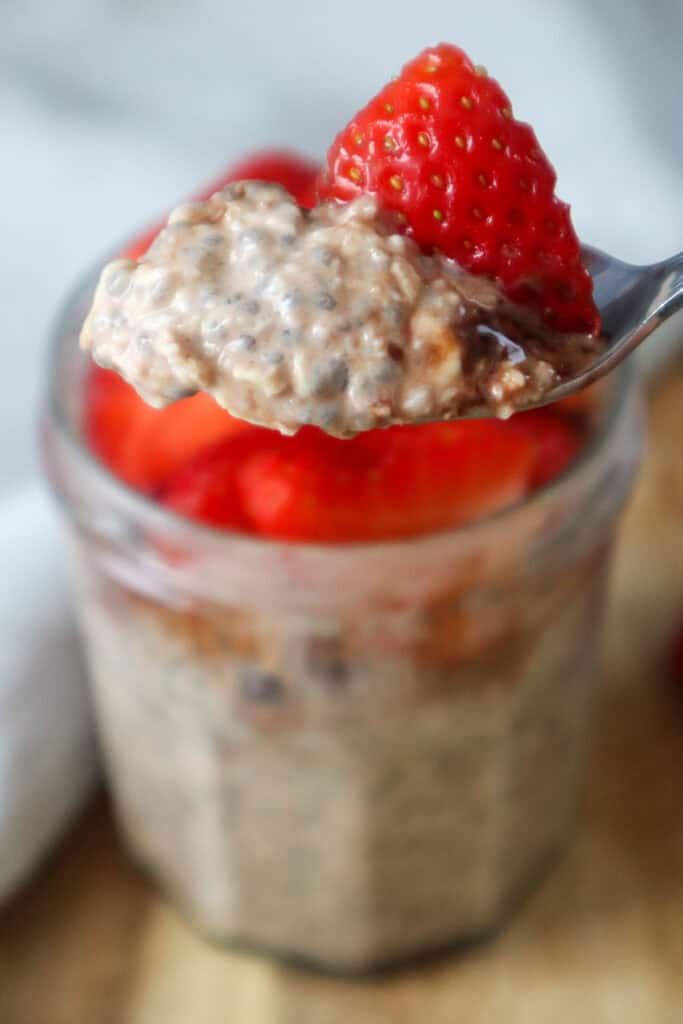 Spoonful of overnight oats with strawberries and fudgy sauce.