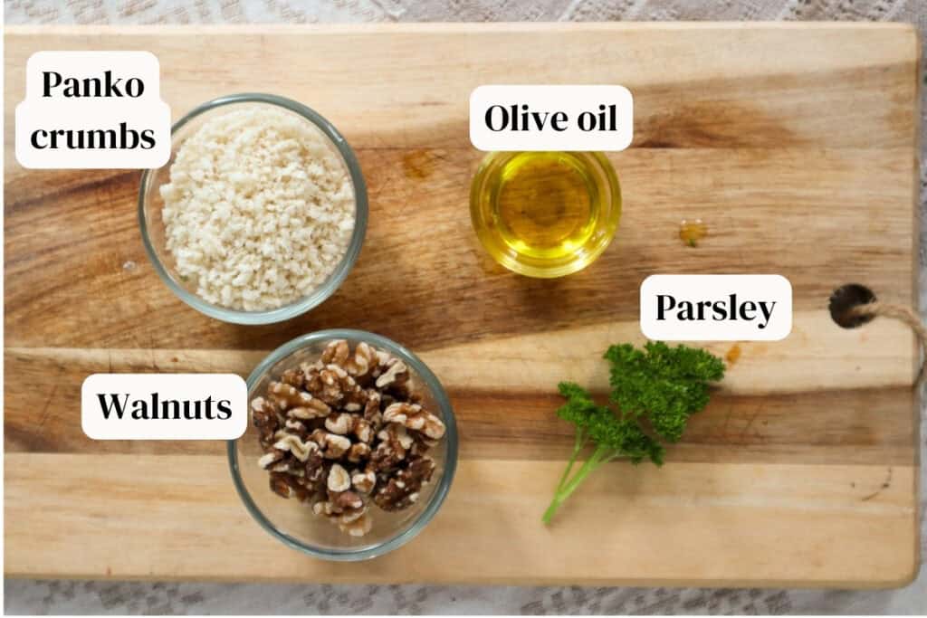 Walnuts, panko crumbs, olive oil in small glass bowls on a wooden board with parsley.