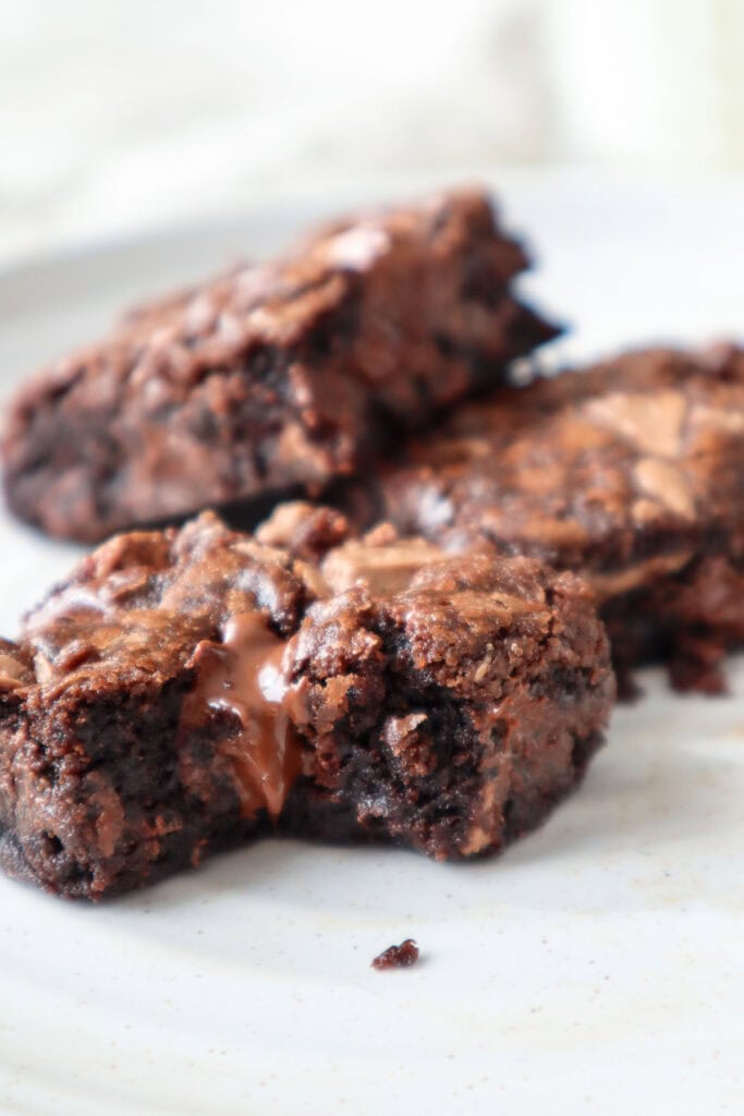 Three chocolate chocolate chip cookie bars on a white plate with a glass of milk in the background.