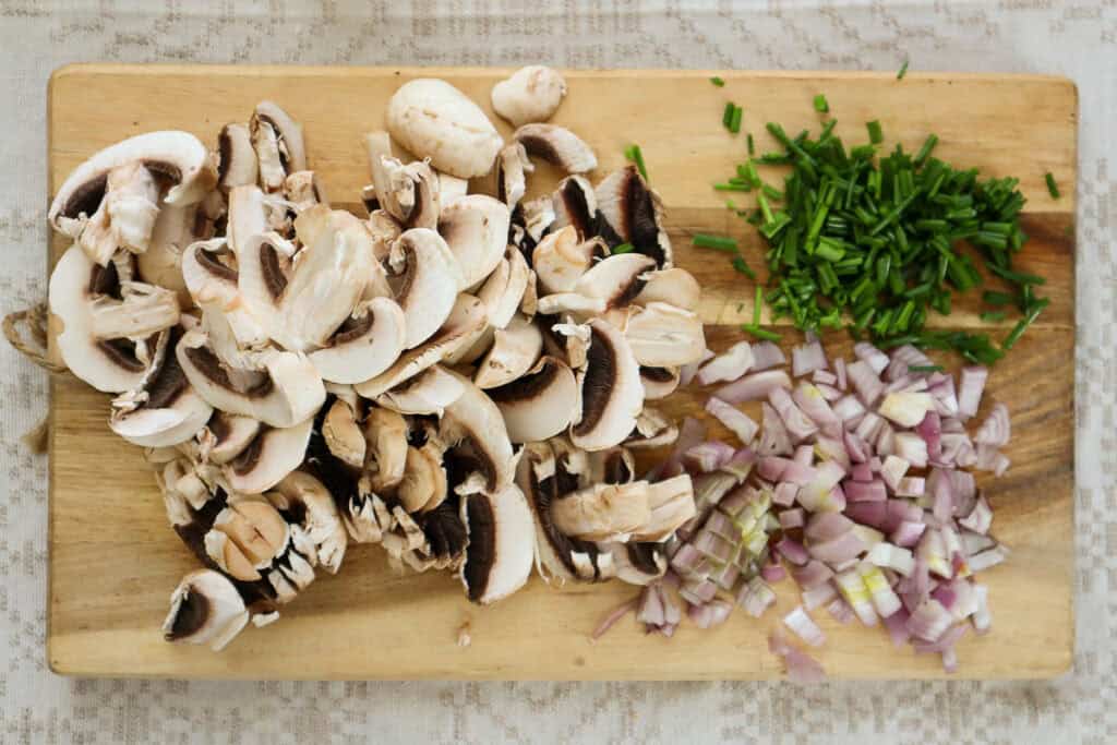 Sliced mushrooms, shallots and chives on wooden board.