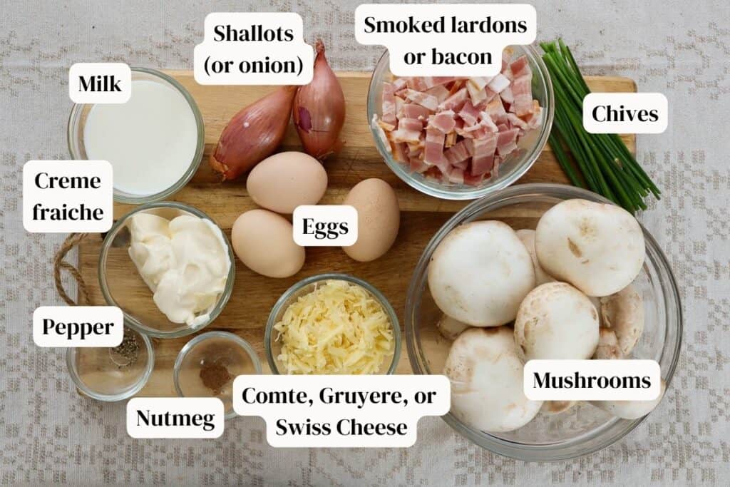 Sliced bacon, shallots, milk, mushrooms, grated cheese, creme fraiche, milk, pepper, nutmeg in small glass bowls, plus bunch of chives and 3 eggs on a wooden board.