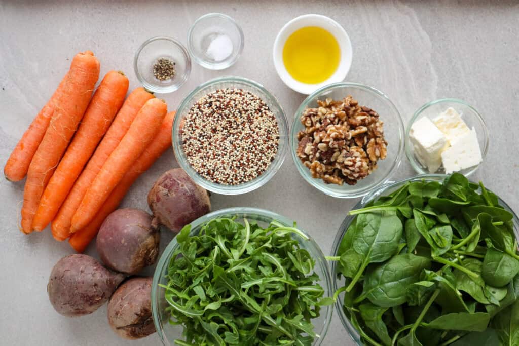 Quinoa, carrots, beets, arugula, baby spinach, walnuts, olive oil, salt, pepper, feta cheese on table.