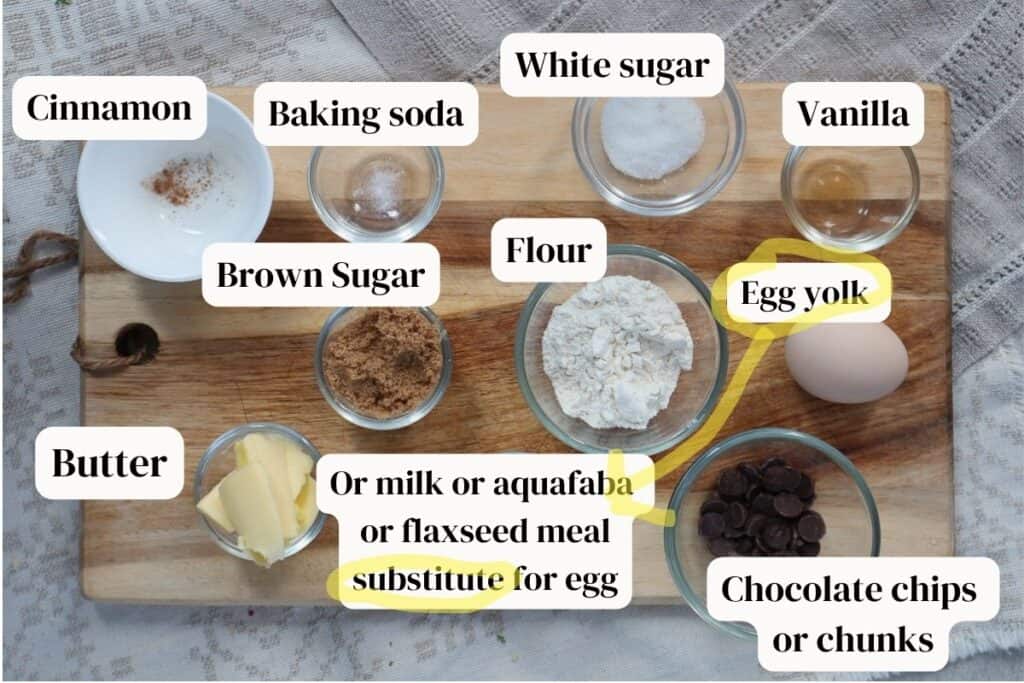 Flour, chocolate chips. egg, vanilla, baking soda, butter, white and brown sugar in small bowls on a wooden board.