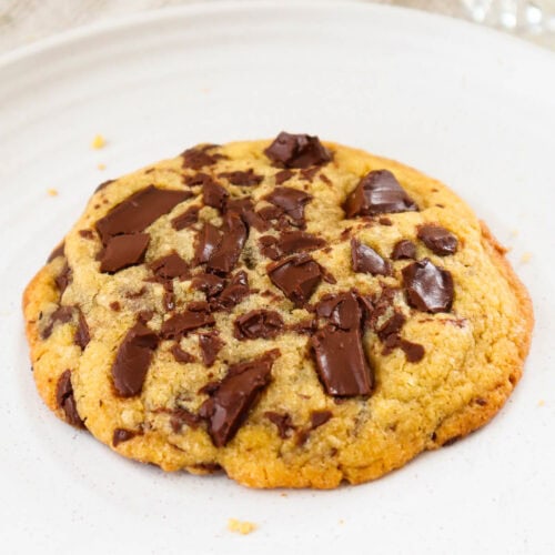 Single chocolate chip cookie with dark chocolate chunks on a beige plate.