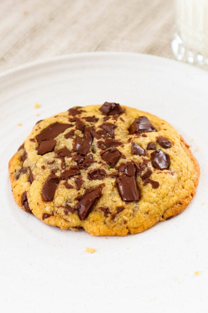 Single chocolate chip cookie with dark chocolate chunks on a beige plate.