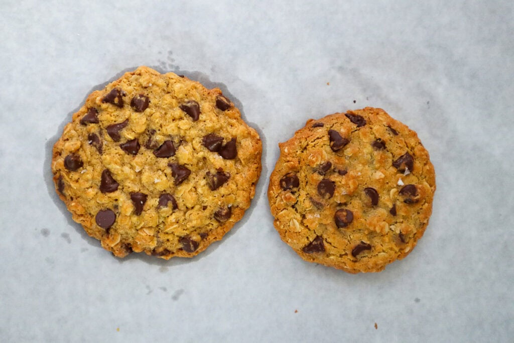 Left oatmeal chocolate chip cookie oven baked and right oatmeal chocolate chip cookie air fryer baked on parchment paper.
