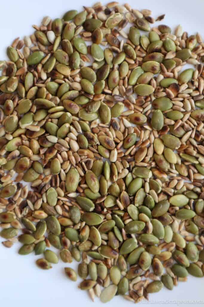 Roasted pumpkin seeds and sunflower seeds on white plate.