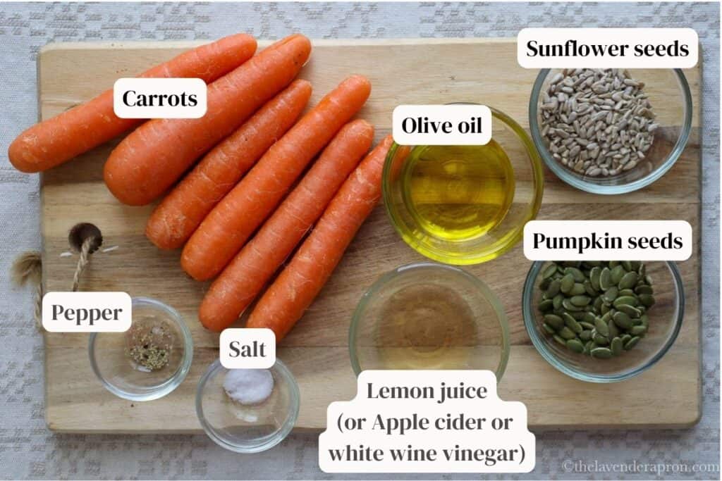 Ingredients to make French carrot salad including carrots, oiive oil, lemon juice, pumpkin seeds, sunflower seeds, salt and pepper on a wooden board.