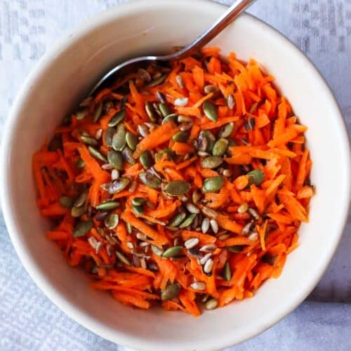 French carrot salad with roasted pumpkin and sesame seeds in bowl with a spoon.