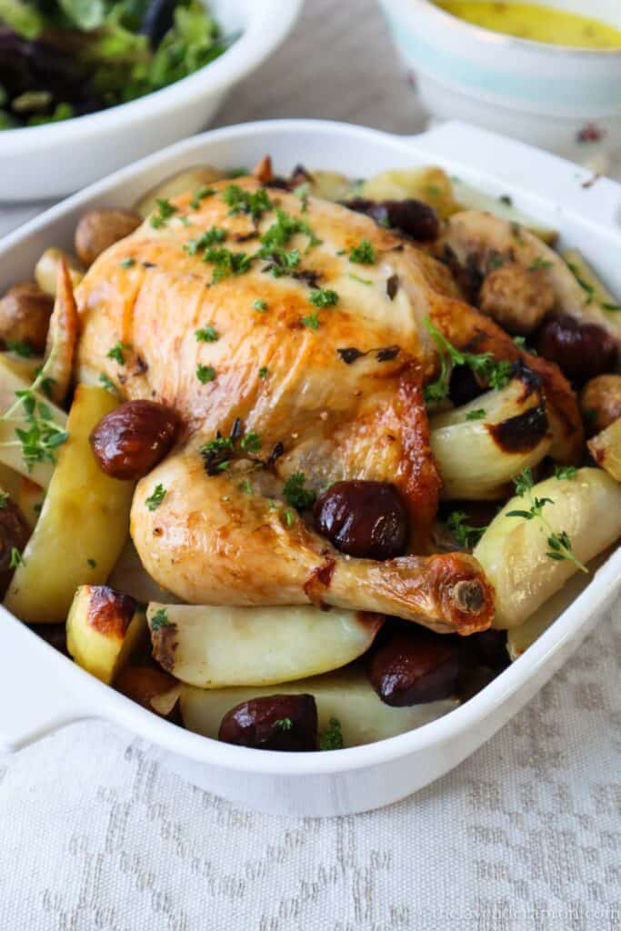 French roast chicken with chestnuts, potatoes and mushrooms in a white roasting pan.