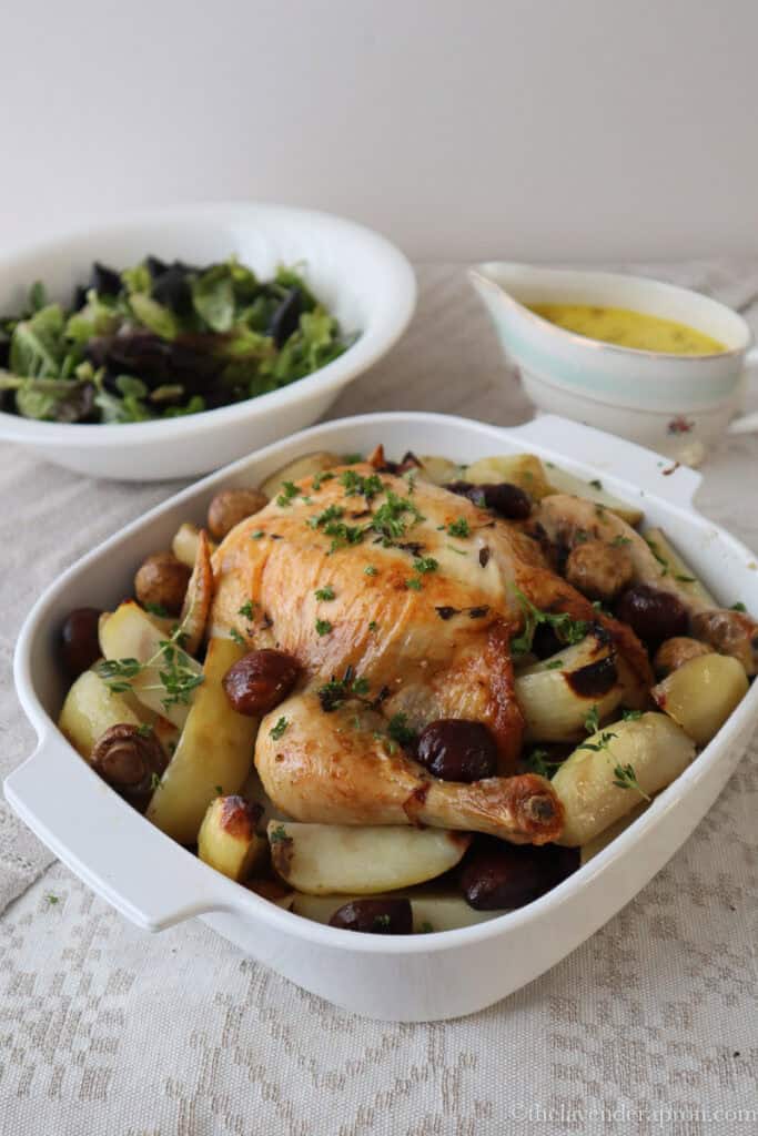 French roast chicken with chestnuts, mushrooms and potatoes with cider sauce on the side in a pouring dish.
