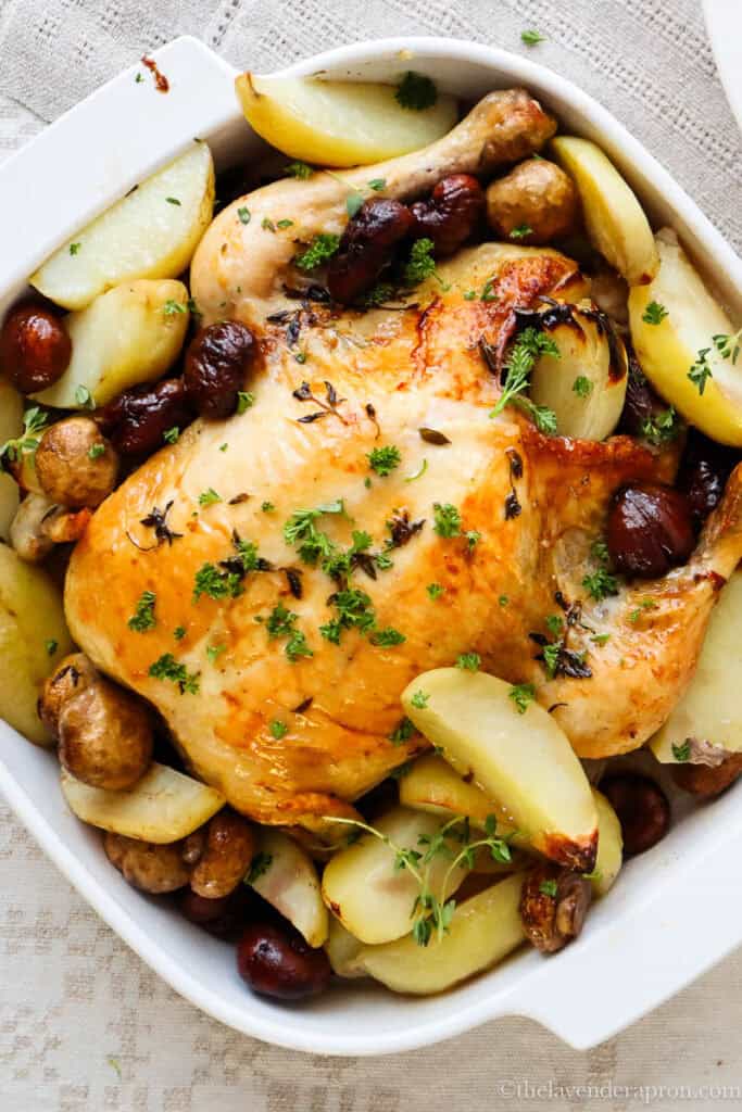 French roasted chicken with thyme, chestnuts, potatoes and mushrooms in a white roasting pan.