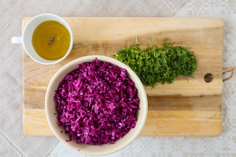 Purple cabbage shredded, finely shopped dill and lemon dressing on wooden board.