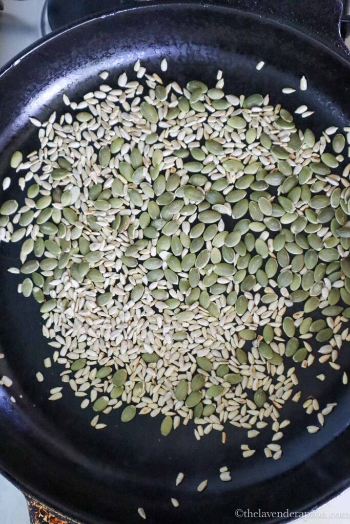 Roasting pumpkin seeds and sunflower seed in black pan.