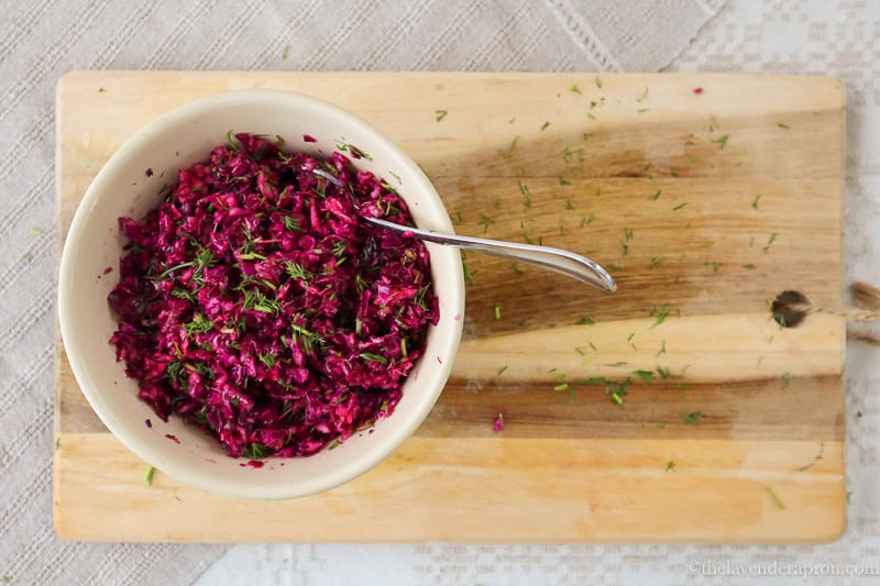 Purple cabbage coleslaw mixed with dill and lemon dressing with a spoon on a wooden board.