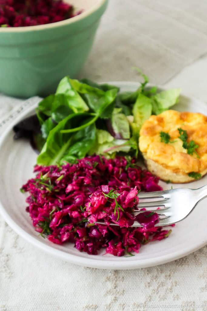 Purple cabbage coleslaw served with mini quiche and green salad on beige plate.